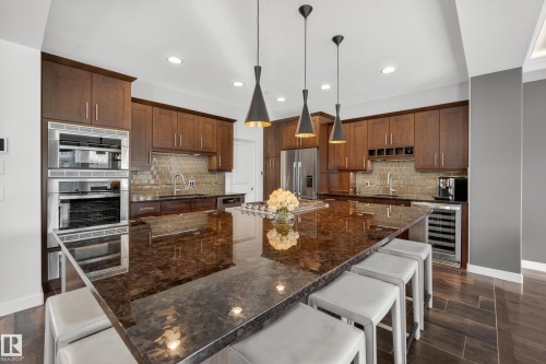 Gourmet kitchen featuring a large central island with stone countertop, stainless steel appliances including a built-in oven and microwave, dark wood cabinetry, and a tile backsplash - 2760 Watcher Way, Edmonton, AB - Indoor Photo Showing Kitchen With Upgraded Kitchen