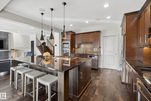Gourmet kitchen featuring a large island with seating, a built-in range, stainless steel appliances, dark wood cabinetry, and wood-finish flooring - 2760 Watcher Way, Edmonton, AB - Indoor Photo Showing Kitchen With Upgraded Kitchen