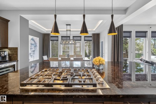 Integrated gas cooktop on a polished stone countertop island, featuring three pendant light fixtures - 2760 Watcher Way, Edmonton, AB - Indoor