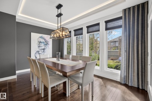 Dining area featuring dark wood-finish flooring, a tray ceiling with recessed lighting, and a multi-pane window wall with individual roller shades - 2760 Watcher Way, Edmonton, AB - Indoor Photo Showing Dining Room