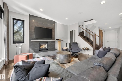 Open-concept living space featuring wood-finish flooring, a contemporary fireplace with a tiled surround, a light-toned mantle, and recessed ceiling lighting - 2760 Watcher Way, Edmonton, AB - Indoor Photo Showing Living Room With Fireplace