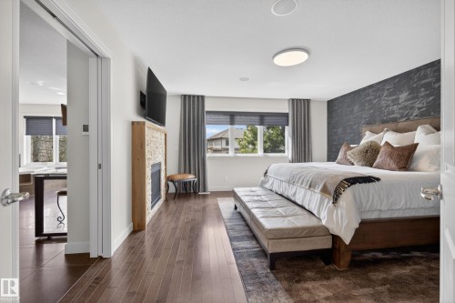 Expansive room featuring rich wood-finish flooring, a contemporary fireplace with a stone surround, and an accent wall with a textured finish - 2760 Watcher Way, Edmonton, AB - Indoor Photo Showing Bedroom