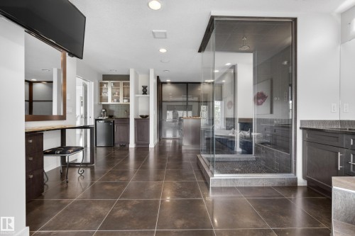 Spacious interior featuring large format tile flooring, a glass-enclosed shower with pebble-finish floor, dark wood cabinetry with stone countertops, a vanity area, and recessed lighting - 2760 Watcher Way, Edmonton, AB - Indoor Photo Showing Other Room