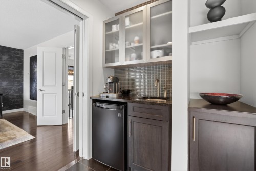 Built-in wet bar featuring dark wood cabinetry, a compact refrigerator, and a mosaic tile backsplash - 2760 Watcher Way, Edmonton, AB - Indoor