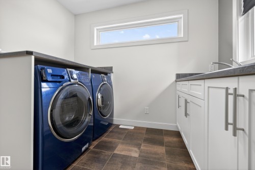 Laundry area featuring white cabinetry, a dark countertop, a stainless steel sink, and a horizontal window - 2760 Watcher Way, Edmonton, AB - Indoor Photo Showing Laundry Room