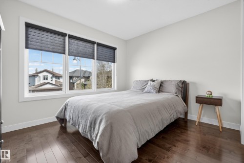 Bedroom featuring wood-finish flooring, white baseboards, and a series of three large windows with dark roller blinds - 2760 Watcher Way, Edmonton, AB - Indoor Photo Showing Bedroom