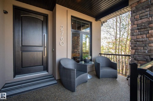 Covered front entry featuring a dark wood-finish door with brushed metal hardware, a large window with black framing, and stone veneer accents - 2760 Watcher Way, Edmonton, AB - Outdoor With Deck Patio Veranda With Exterior