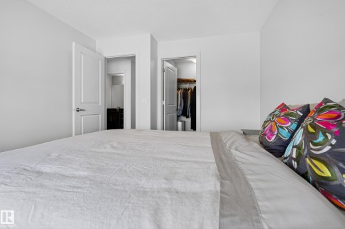 Spacious bedroom featuring white walls and doors, a built-in closet with shelving, and an en-suite bathroom with a dark wood vanity and mirror - 2760 Watcher Way, Edmonton, AB - Indoor Photo Showing Bedroom