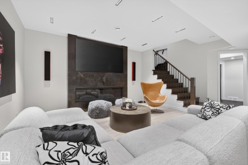 Contemporary living space featuring a linear fireplace with a dark stone-look surround, integrated television, recessed lighting, and light wood-finish flooring - 2760 Watcher Way, Edmonton, AB - Indoor