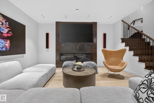 Integrated fireplace with a dark-toned surround, hardwood flooring, recessed lighting, and a dark wood staircase with metal balusters - 2760 Watcher Way, Edmonton, AB - Indoor Photo Showing Living Room With Fireplace