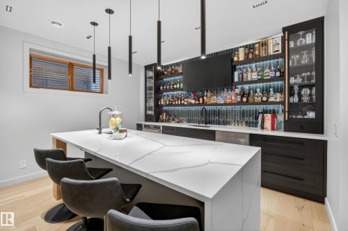 Custom bar featuring a waterfall-edge island with a stone countertop, built-in cabinetry, integrated shelving with under-shelf lighting, and a tile backsplash - 2760 Watcher Way, Edmonton, AB - Indoor Photo Showing Other Room