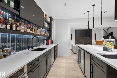Wet bar featuring quartz countertops, dark cabinetry, a black sink with a matte black faucet, and a tiled backsplash with integrated lighting - 2760 Watcher Way, Edmonton, AB - Indoor Photo Showing Kitchen