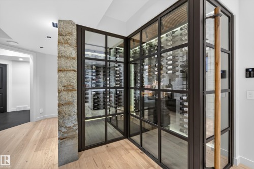 Modern wine cellar featuring glass and dark metal framing, illuminated bottle racks, and a natural wood door handle - 2760 Watcher Way, Edmonton, AB - Indoor Photo Showing Other Room