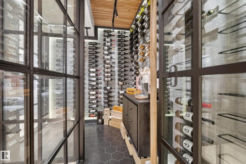 Custom wine cellar featuring floor-to-ceiling glass paneling, hexagonal tile flooring, extensive wall-mounted bottle storage, a built-in credenza, and a slatted wood ceiling - 2760 Watcher Way, Edmonton, AB - Indoor Photo Showing Other Room