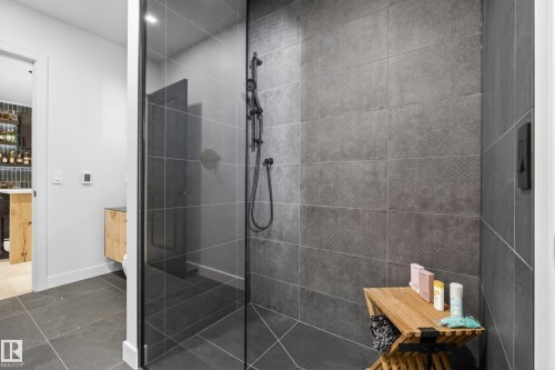 Walk-in shower featuring dark-toned large format tile walls and floor, clear glass enclosure, and a black matte shower fixture - 2760 Watcher Way, Edmonton, AB - Indoor Photo Showing Bathroom