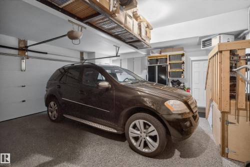 Spacious garage featuring a durable epoxy floor, overhead storage racks, a white paneled garage door, built-in shelving, and a finished staircase with wooden railing - 2760 Watcher Way, Edmonton, AB - Indoor Photo Showing Garage