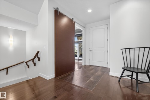 Entryway featuring a large sliding barn door with exposed hardware, wood-finish flooring, a contemporary wall sconce, and a two-panel interior door - 2760 Watcher Way, Edmonton, AB - Indoor Photo Showing Other Room
