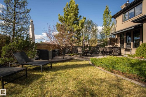 Expansive backyard featuring a manicured lawn, stone-paved patio, built-in outdoor kitchen, mature trees, and a privacy hedge - 2760 Watcher Way, Edmonton, AB - Outdoor With Deck Patio Veranda