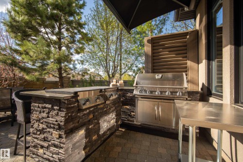 Outdoor kitchen featuring a built-in stainless steel grill, stacked stone facade, integrated bar seating, and paver patio - 2760 Watcher Way, Edmonton, AB - Outdoor With Exterior