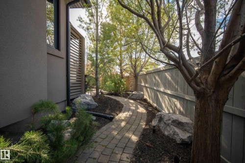 Landscaped side yard featuring a paver stone pathway, mature trees, and decorative boulders - 2760 Watcher Way, Edmonton, AB - Outdoor