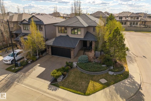 Contemporary exterior featuring a neutral stucco and stone facade, dark-framed windows, an attached two-car garage, and a concrete driveway - 2760 Watcher Way, Edmonton, AB - Outdoor With Facade