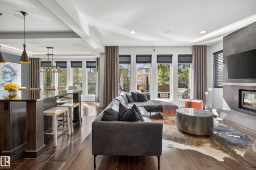 Open-concept living area featuring rich wood-finish flooring, a contemporary fireplace with a tiled surround, and multiple large windows - 2760 Watcher Way, Edmonton, AB - Indoor Photo Showing Living Room With Fireplace