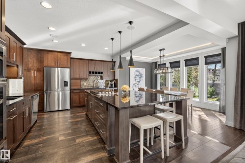 Gourmet kitchen featuring dark wood cabinetry, stainless steel appliances, and a large central island with seating - 2760 Watcher Way, Edmonton, AB - Indoor Photo Showing Kitchen With Upgraded Kitchen