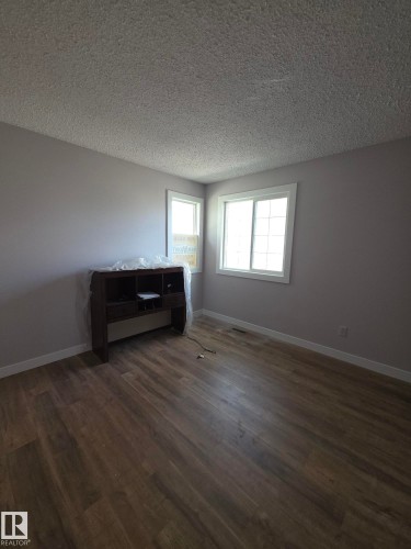 Room featuring wood-finish flooring, two windows, light gray walls, white baseboards, and a textured ceiling - 16 South Ram Crescent, Devon, AB - Indoor