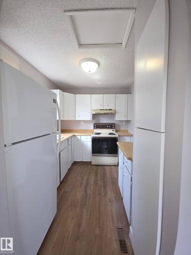 Galley kitchen featuring wood-finish flooring, white cabinetry, light wood-finish countertops, and a white appliance package - 16 South Ram Crescent, Devon, AB - Indoor Photo Showing Kitchen