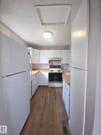 Galley kitchen featuring wood-finish flooring, white cabinetry, light wood-finish countertops, and a white appliance package - 