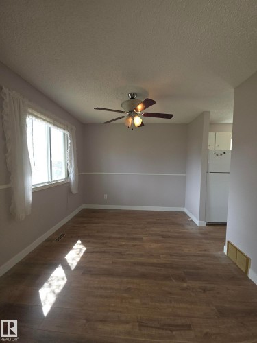 Spacious room featuring wood-finish flooring, a ceiling fan with integrated lighting, and a large window with white trim - 16 South Ram Crescent, Devon, AB - Indoor Photo Showing Other Room