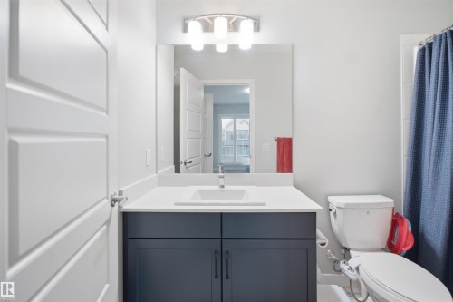 Bathroom featuring a vanity with a white countertop, undermount sink, dark cabinetry with dark hardware, and a wall-mounted light fixture - 2284 Chokecherry Close, Edmonton, AB - Indoor Photo Showing Bathroom