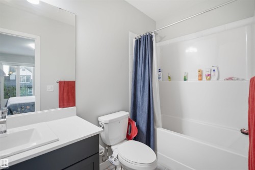 Bathroom featuring a single vanity with a white countertop and dark cabinetry, an undermount rectangular sink, a wall-mounted mirror, a toilet, and a white shower-over-tub combination with a shower rod - 2284 Chokecherry Close, Edmonton, AB - Indoor Photo Showing Bathroom