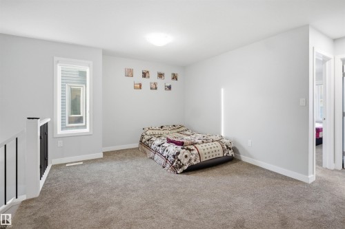 Spacious carpeted room featuring a large window, contemporary ceiling light fixture, white baseboards, and a doorway leading to an additional space - 2284 Chokecherry Close, Edmonton, AB - Indoor Photo Showing Bedroom