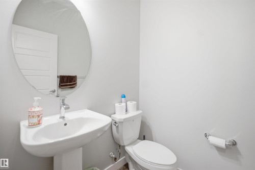Powder room featuring a pedestal sink with a chrome faucet, an oval wall mirror, and a white toilet - 2284 Chokecherry Close, Edmonton, AB - Indoor Photo Showing Bathroom