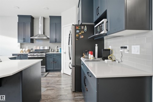 Modern kitchen featuring dark cabinetry with black hardware, light quartz countertops, a stainless steel range with matching hood, and wood-finish flooring - 2284 Chokecherry Close, Edmonton, AB - Indoor Photo Showing Kitchen With Upgraded Kitchen