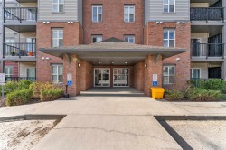 Brick and siding exterior featuring a covered entryway with columns, glass entry doors, multiple windows, and upper-level balconies with black railings - 