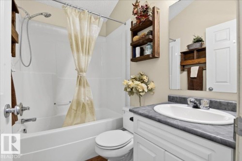 Bathroom featuring a white vanity with a dark countertop and an oval sink, a toilet, and a bathtub with a shower head and a shower curtain - 3518 18 Street, Edmonton, AB - Indoor Photo Showing Bathroom