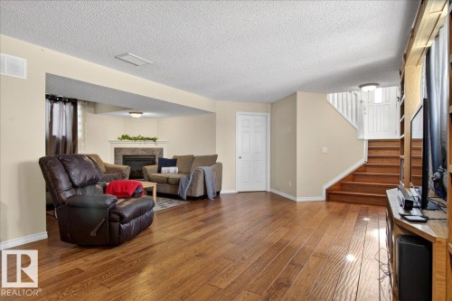 Living area featuring hardwood flooring, a fireplace with a stone surround, and a staircase with wooden treads and white risers - 3518 18 Street, Edmonton, AB - Indoor Photo Showing Living Room