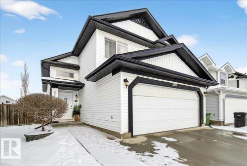 The property features white siding with black trim, a prominent garage, and a snow-covered front yard with a tree - 3518 18 Street, Edmonton, AB - Outdoor