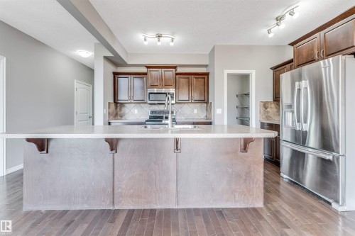 Kitchen featuring a central island with an extended countertop, stainless steel appliances, dark wood cabinetry, a tile backsplash, and wood-finish flooring - 2138 32B Street, Edmonton, AB - Indoor Photo Showing Kitchen With Stainless Steel Kitchen With Upgraded Kitchen