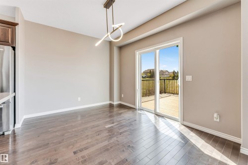 Spacious room featuring wood-finish flooring, a modern linear pendant light fixture, and neutral wall tones - 2138 32B Street, Edmonton, AB - Indoor