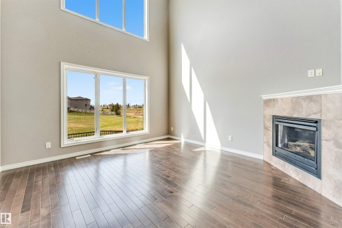 Spacious living area featuring high ceilings, wood-finish flooring, a contemporary fireplace with a tiled surround, and large windows providing abundant natural light - 2138 32B Street, Edmonton, AB - Indoor Photo Showing Living Room With Fireplace