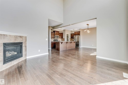 Spacious interior featuring high ceilings, wood-finish flooring, a tile-surround fireplace, an open kitchen, and a central island with bar seating - 2138 32B Street, Edmonton, AB - Indoor Photo Showing Living Room With Fireplace