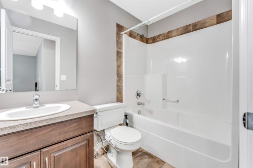 Bathroom featuring a wood-finish vanity with an oval basin, a speckled countertop, a large mirror, a chrome single-handle faucet, and overhead bar lighting - 2138 32B Street, Edmonton, AB - Indoor Photo Showing Bathroom
