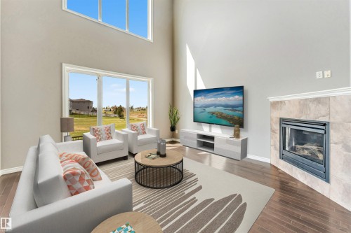 Living area featuring a two-story ceiling, wood-finish flooring, a fireplace with a tiled surround, and large windows with a transom window above - 2138 32B Street, Edmonton, AB - Indoor Photo Showing Living Room With Fireplace