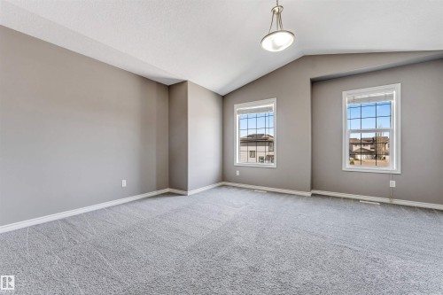 Spacious room featuring vaulted ceilings, a suspended light fixture, two double-paned windows with horizontal blinds, neutral wall paint, and gray patterned carpeting - 2138 32B Street, Edmonton, AB - Indoor Photo Showing Other Room