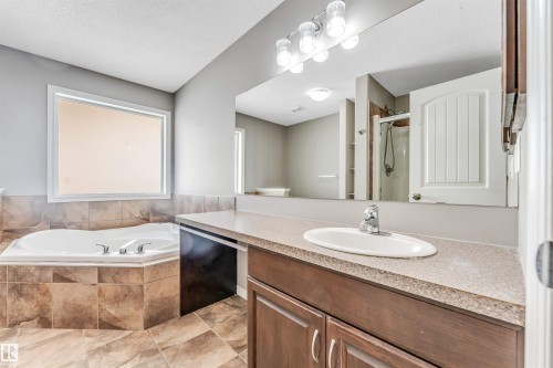 Bathroom featuring a built-in corner soaking tub with tiled surround, a vanity with an integrated sink and laminate countertop, and wood-finish cabinetry - 2138 32B Street, Edmonton, AB - Indoor Photo Showing Bathroom