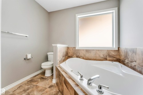 Soaking tub with chrome fixtures, surrounded by earth-toned tilework - 2138 32B Street, Edmonton, AB - Indoor Photo Showing Bathroom