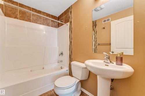 Bathroom featuring a pedestal sink with a chrome faucet, a white tub/shower combination, and complementary brown floor and shower wall tiles - 2138 32B Street, Edmonton, AB - Indoor Photo Showing Bathroom
